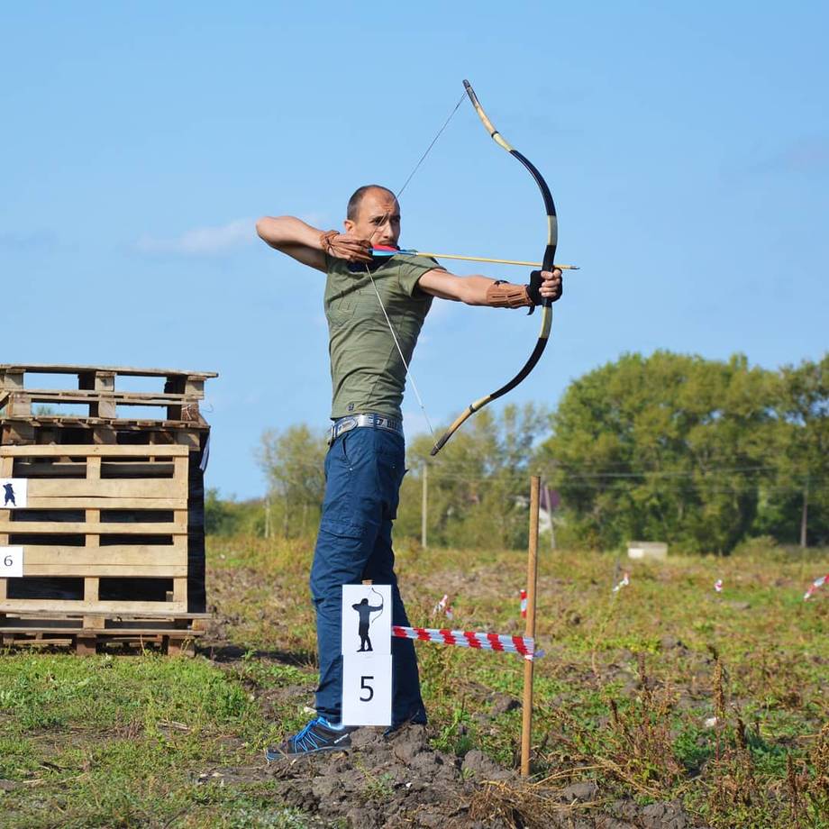 Archer in action at outdoor archery range with target and woodland backdrop