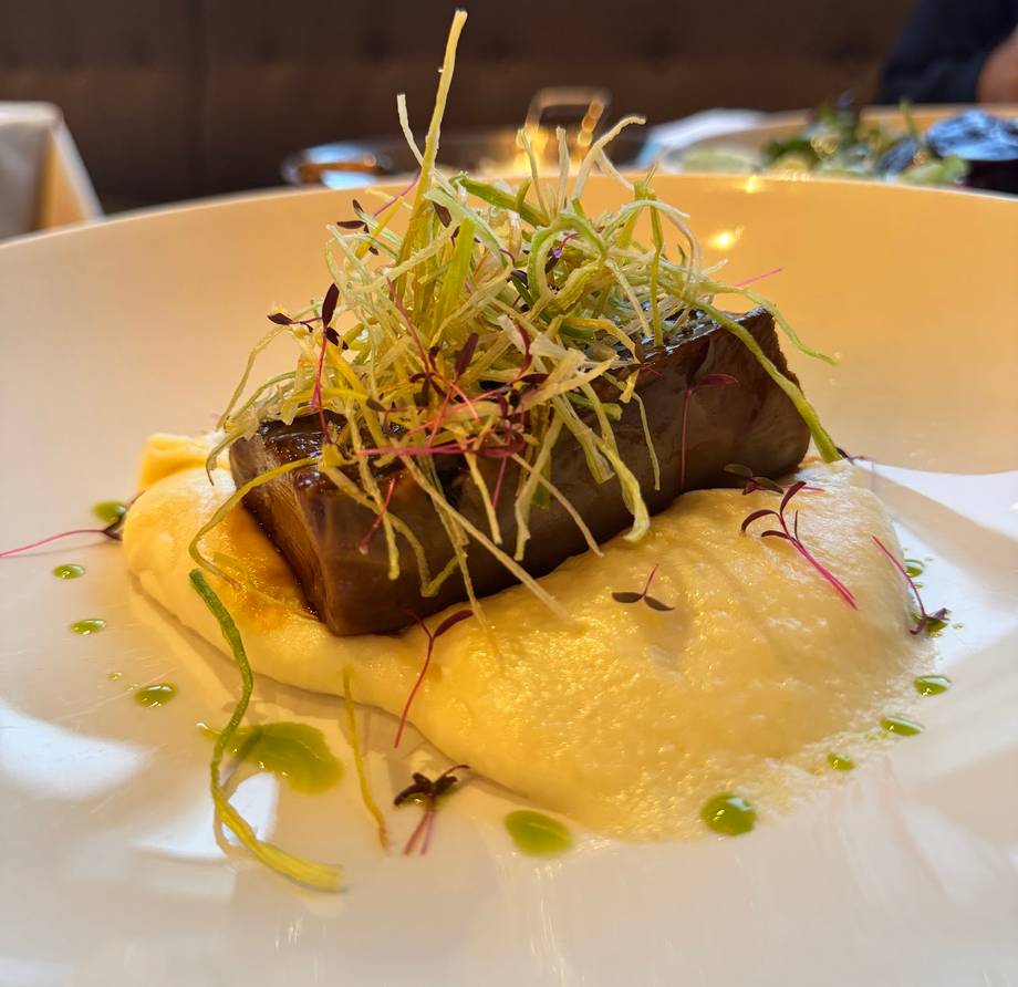 Plated fine dining dish with seared protein and microgreens on yellow sauce