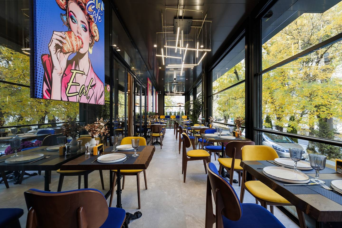 Modern restaurant interior with blue and yellow seating, artwork, and floor-to-ceiling windows