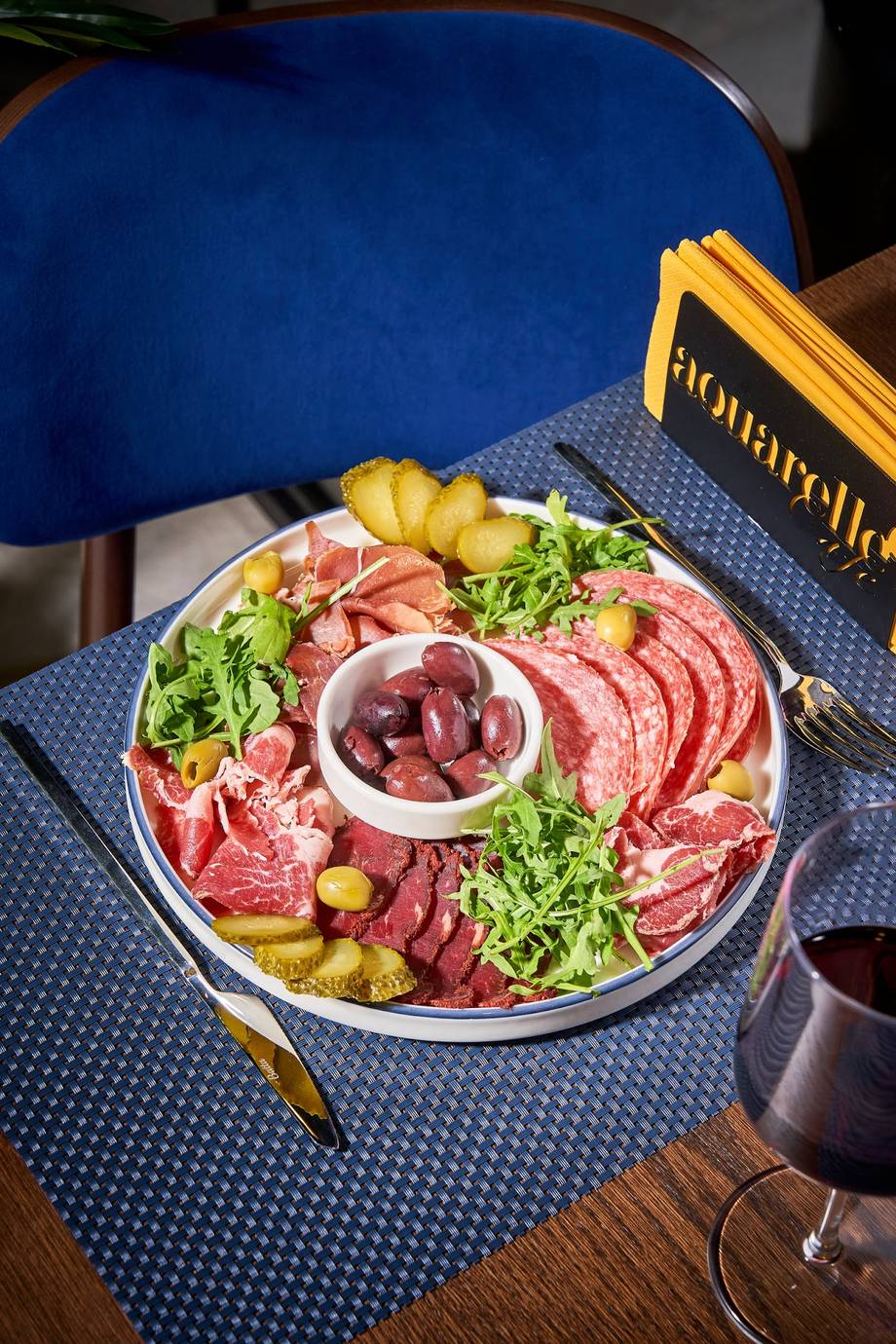 Charcuterie platter with cured meats, pickles, and greens at table