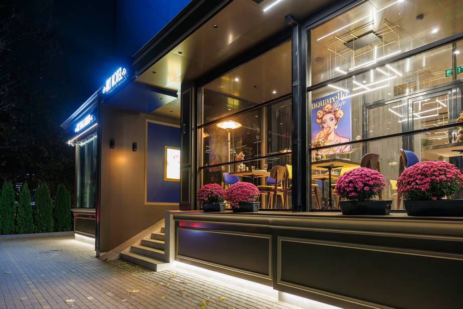Modern storefront exterior with illuminated signage and flower-adorned entrance at dusk