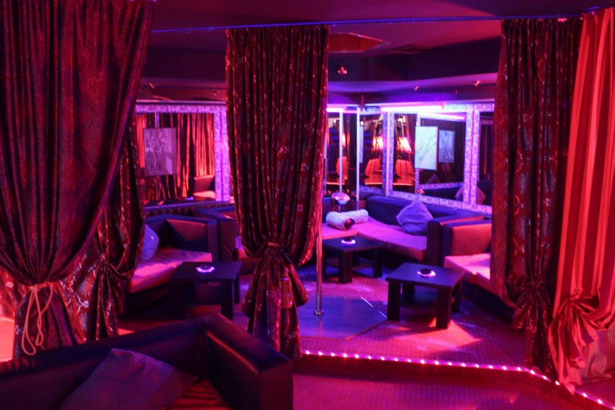VIP lounge with neon pink lighting, draped curtains, and ambient seating areas