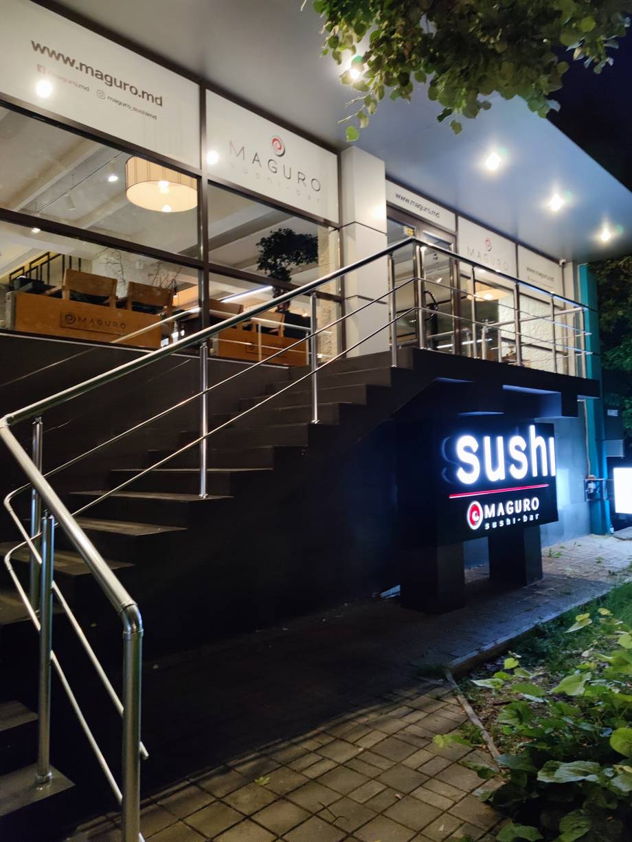 Sushi restaurant storefront with illuminated signage and modern entrance ramp at dusk