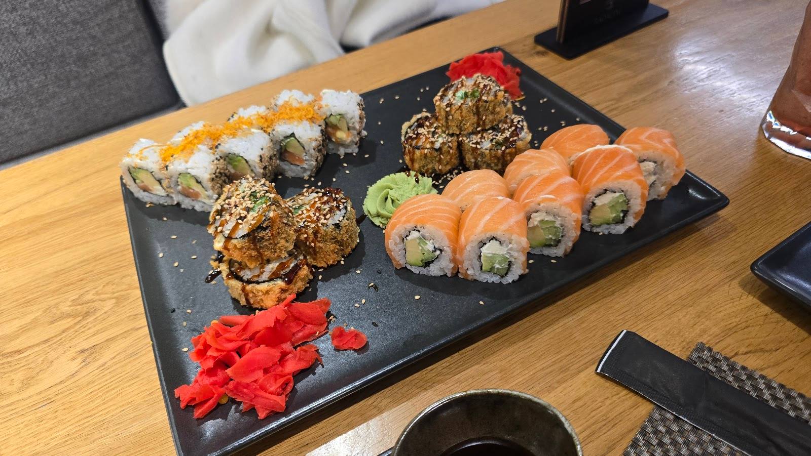 Assorted sushi rolls on black slate platter with ginger and wasabi