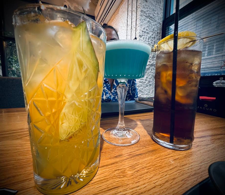 Three craft cocktails with ice and citrus garnish on wooden bar counter
