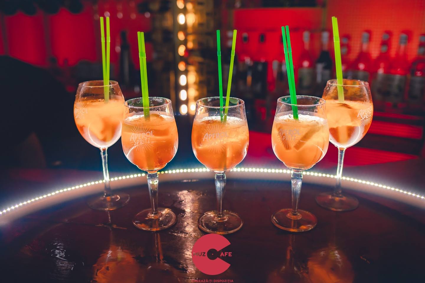 Orange cocktails with straws on illuminated bar counter with ambient red lighting.