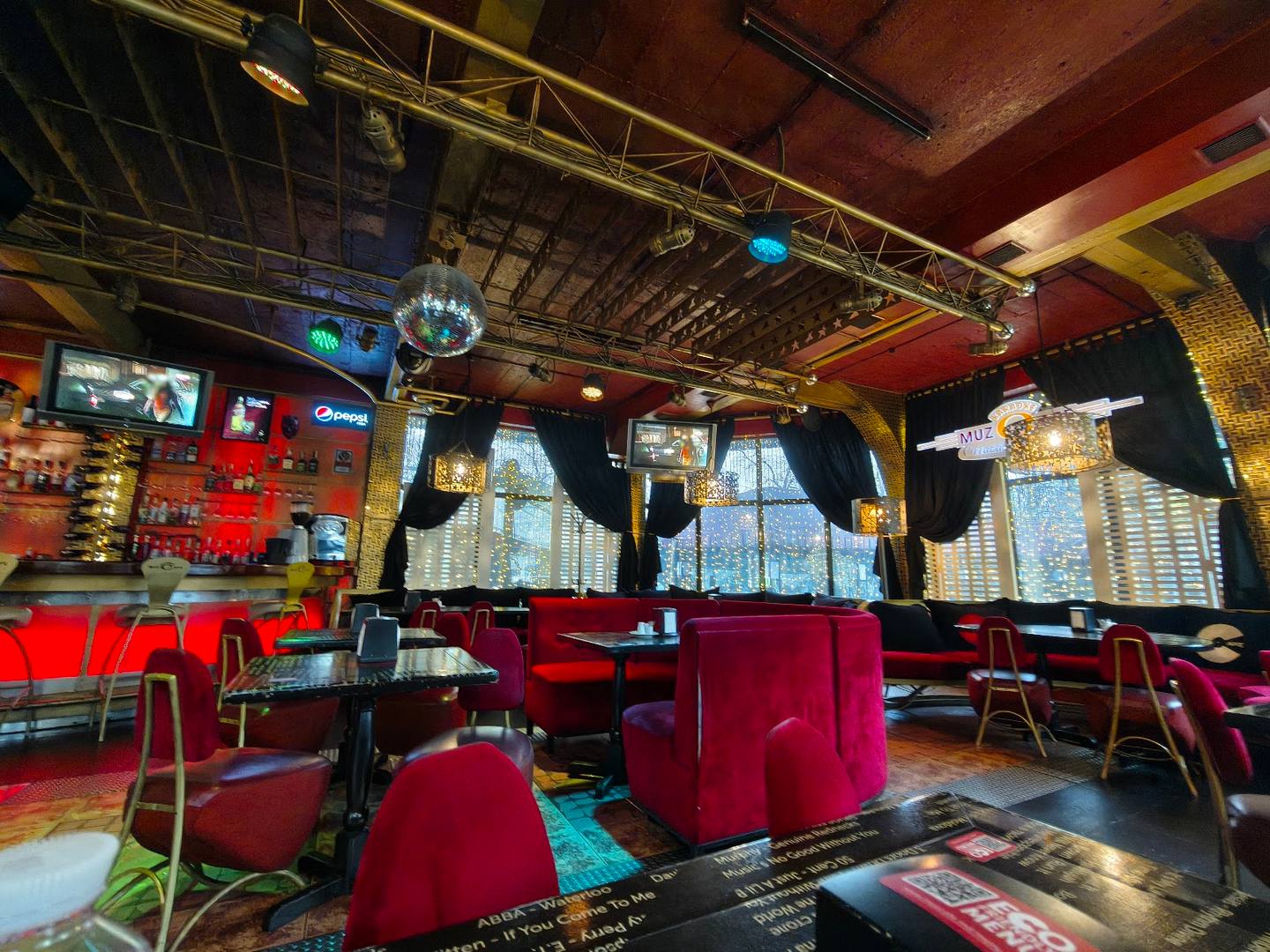 Modern bar lounge with red velvet seating, skyline views, and dynamic industrial ceiling design