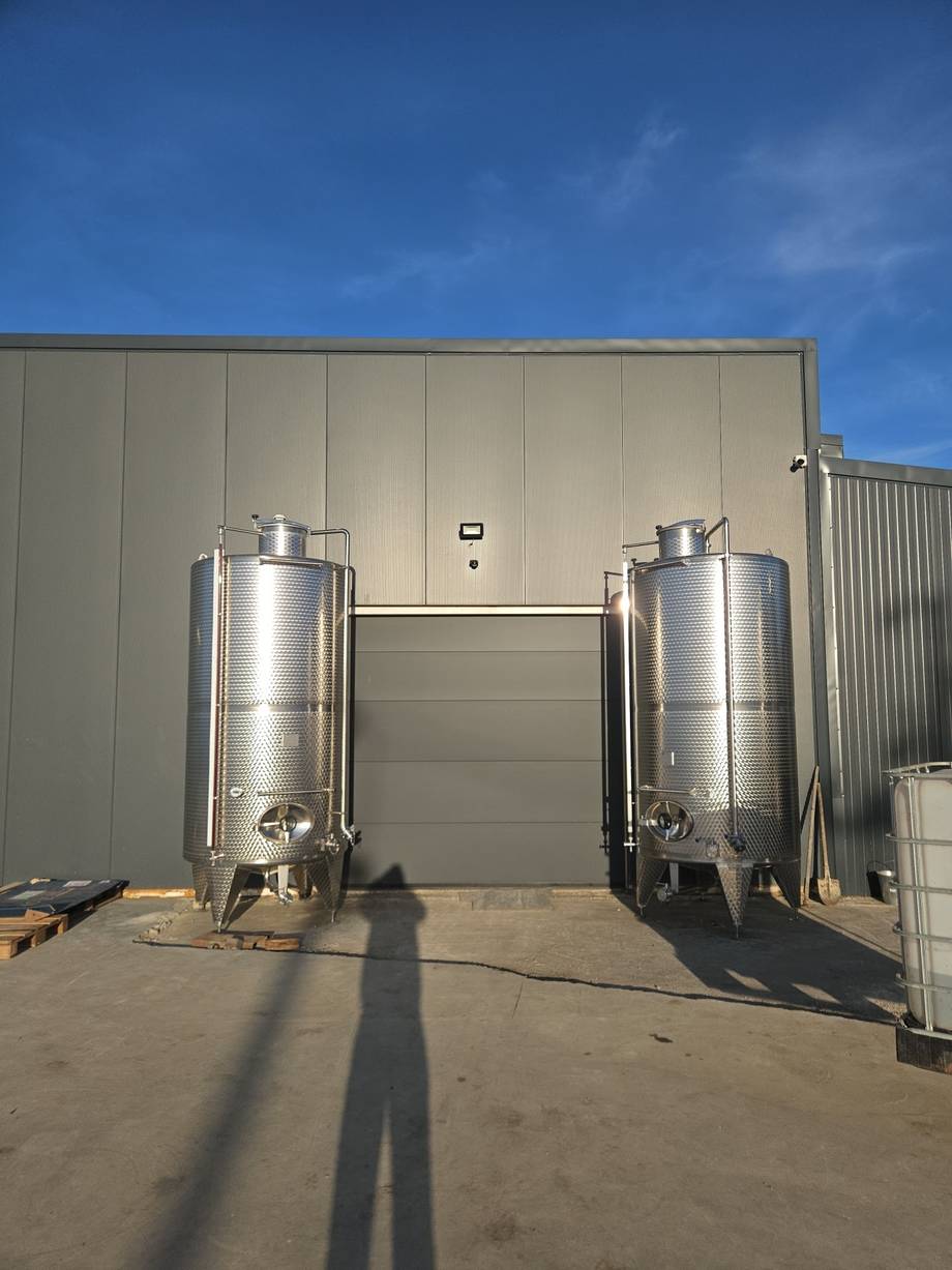 Stainless steel fermentation tanks at a winery facility with industrial warehouse building