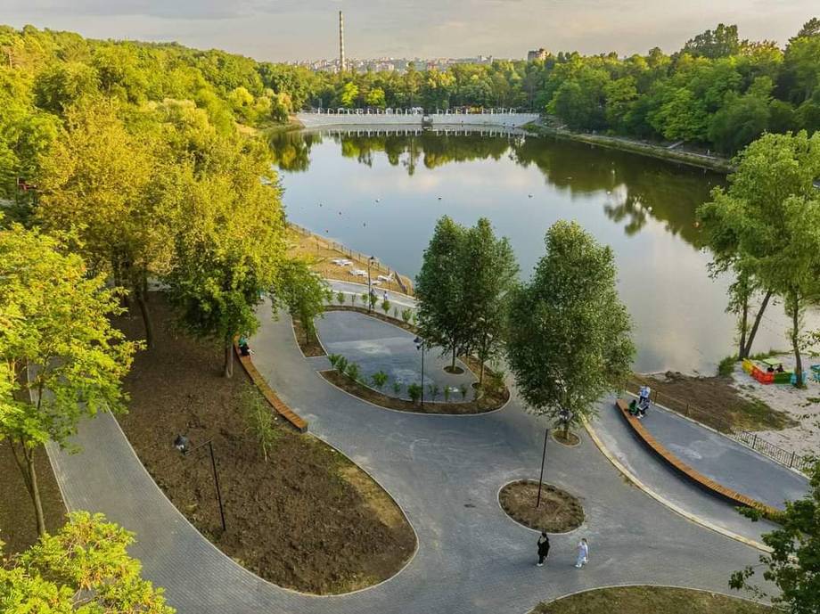 Aerial view of riverside park with curved pathways, landscaping, and water reflection