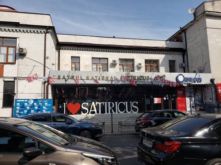 Satiricus storefront with street-level signage and parked vehicles