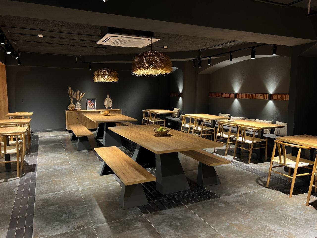 Modern dining space with wooden tables and benches, dark walls, and warm accent lighting
