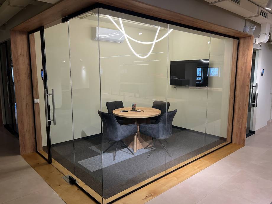 Modern glass-walled meeting room with round wood table and comfortable seating