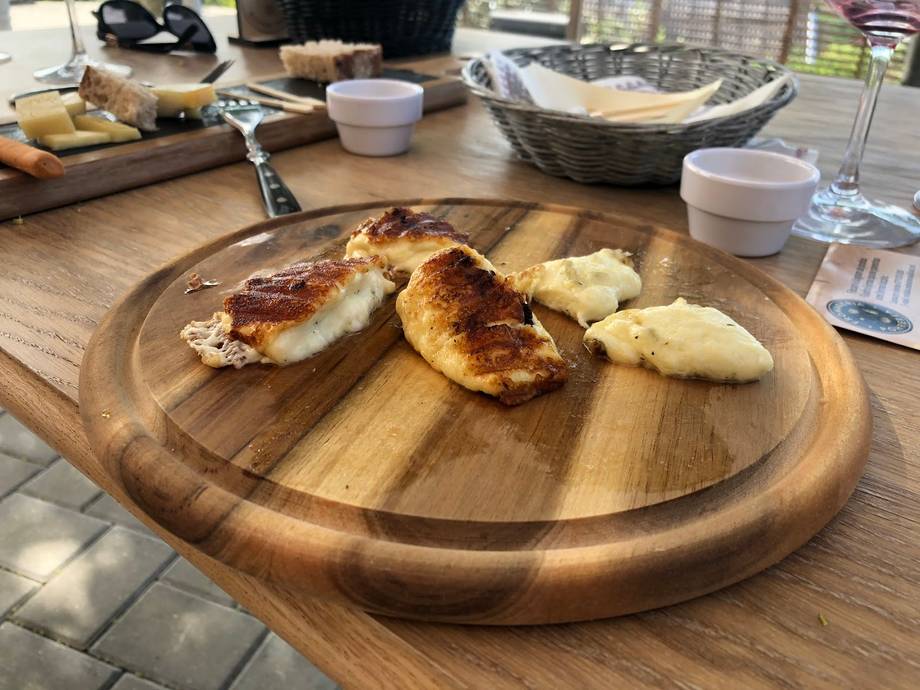 Cheese-topped cured meat slices on wooden serving board with white bowls and table setting