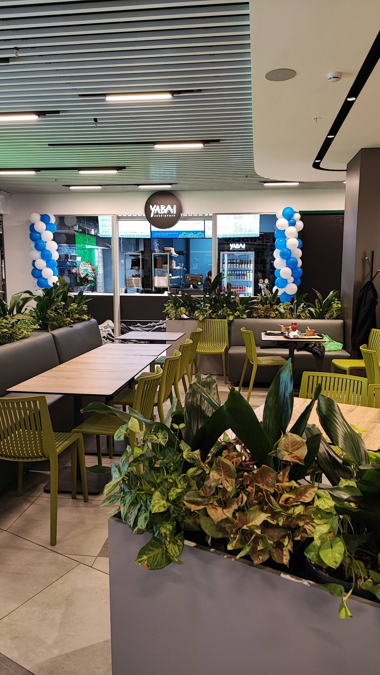 Modern cafe interior with yellow chairs, large windows, and decorative blue balloon arrangement