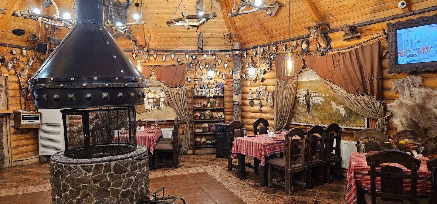 Rustic tavern interior with ornamental fireplace, wooden beamed ceiling, and pink-checked tablecloths