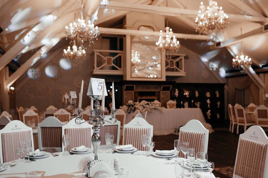 Elegant reception hall with exposed beams, crystal chandeliers, and formally set tables