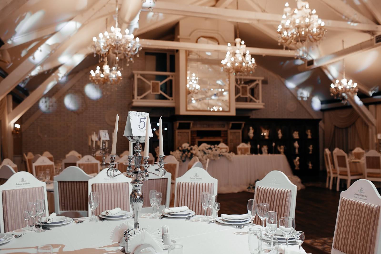 Elegant reception hall with exposed beams, crystal chandeliers, and formally set tables