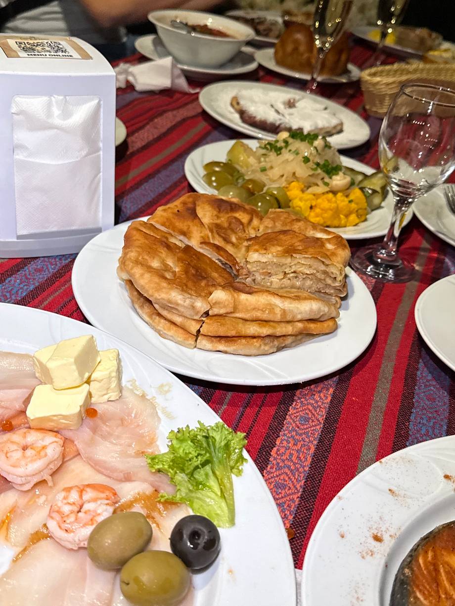 Traditional Moldovan feast with grilled meats, fresh vegetables, and appetizers on red patterned tablecloth