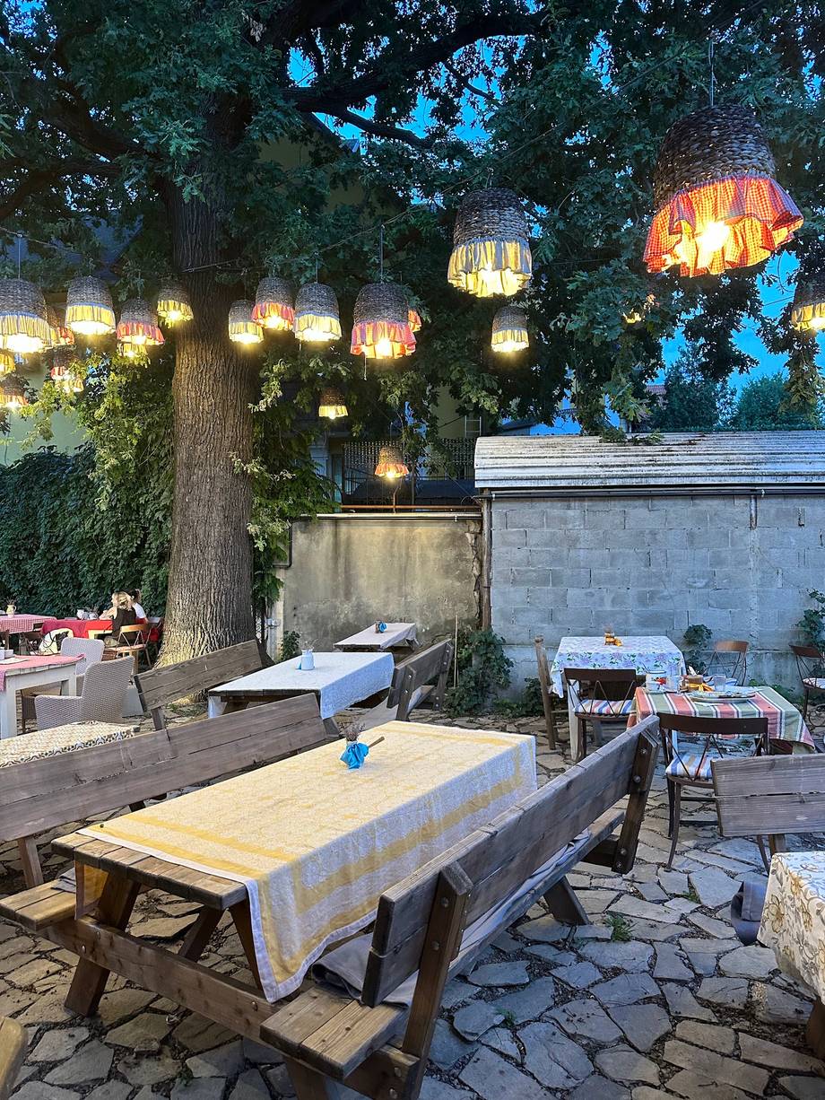 Rustic outdoor terrace with hanging lanterns and dining tables under ancient tree at dusk