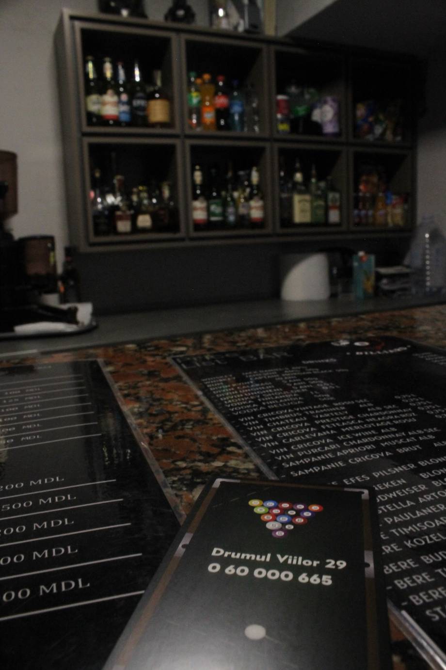 Bar counter with menu cards and backlit bottle display wall