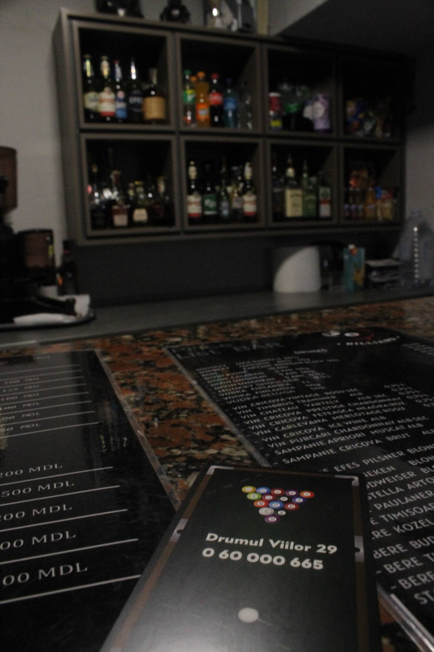 Bar counter with menu cards and backlit bottle display wall