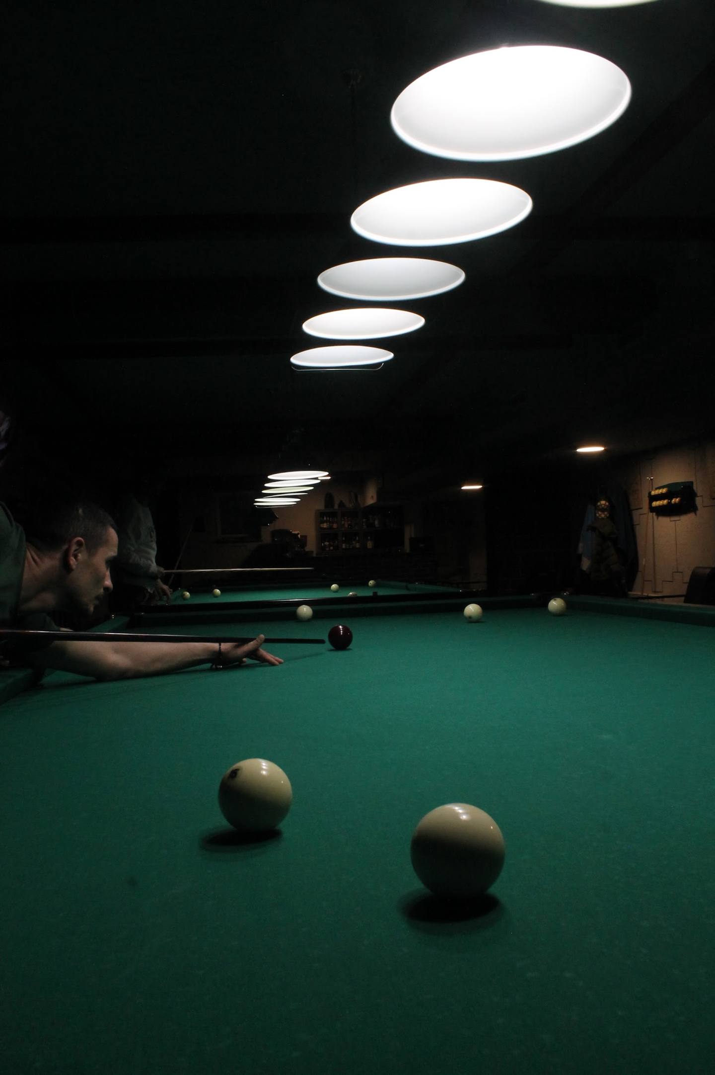 Player shooting pool in dimly lit billiards hall with overhead lighting