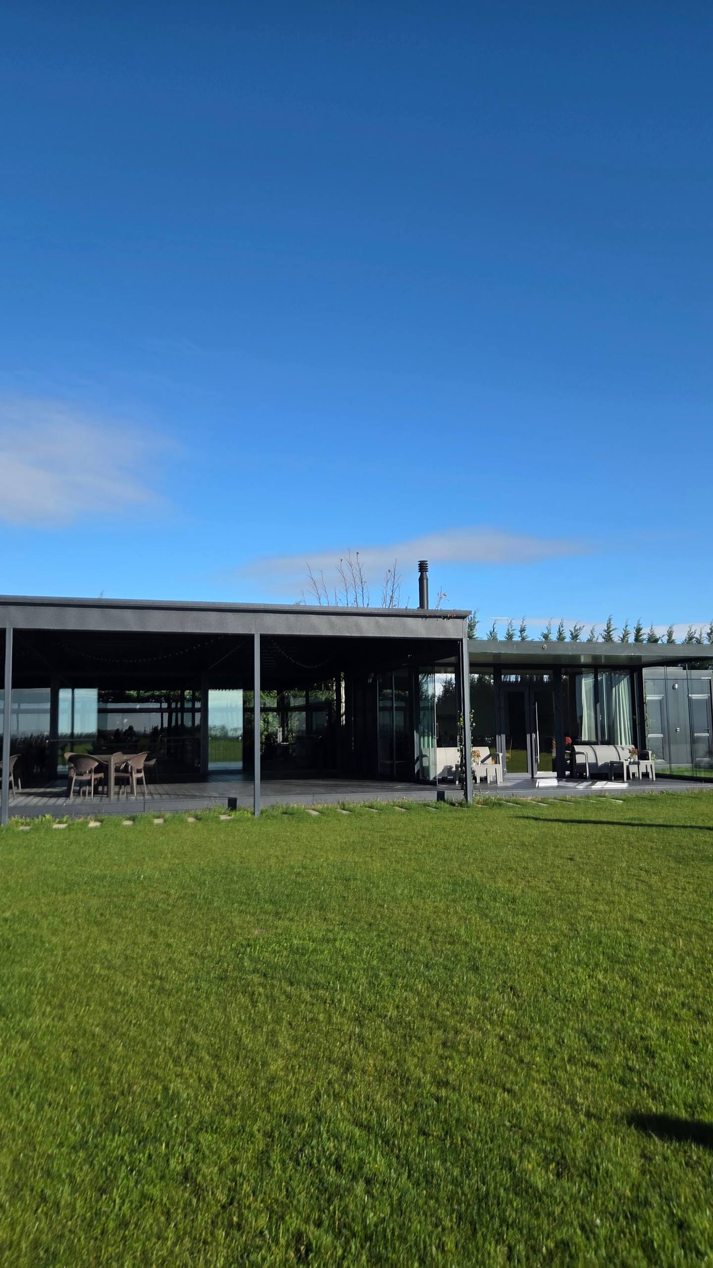 Modern black glass pavilion with terrace seating and manicured lawn, set against forest backdrop