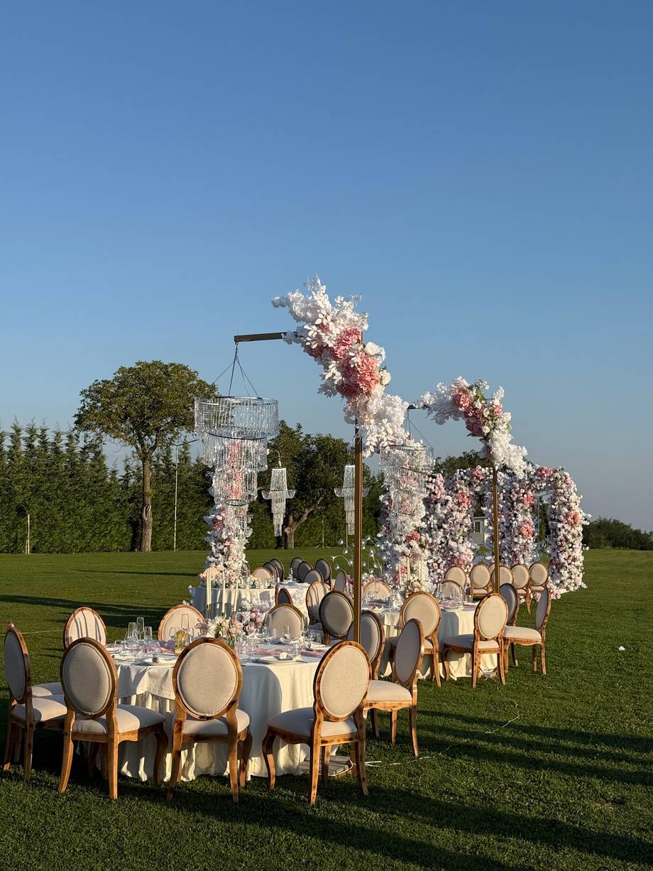 Open-air wedding reception with floral arch and round tables on manicured lawn venue
