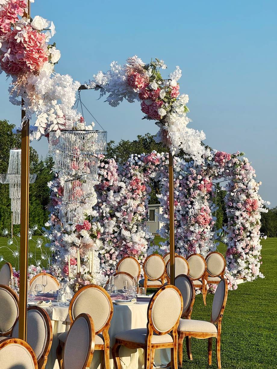 Floral arch ceremony setup with rose-wood chairs on outdoor lawn