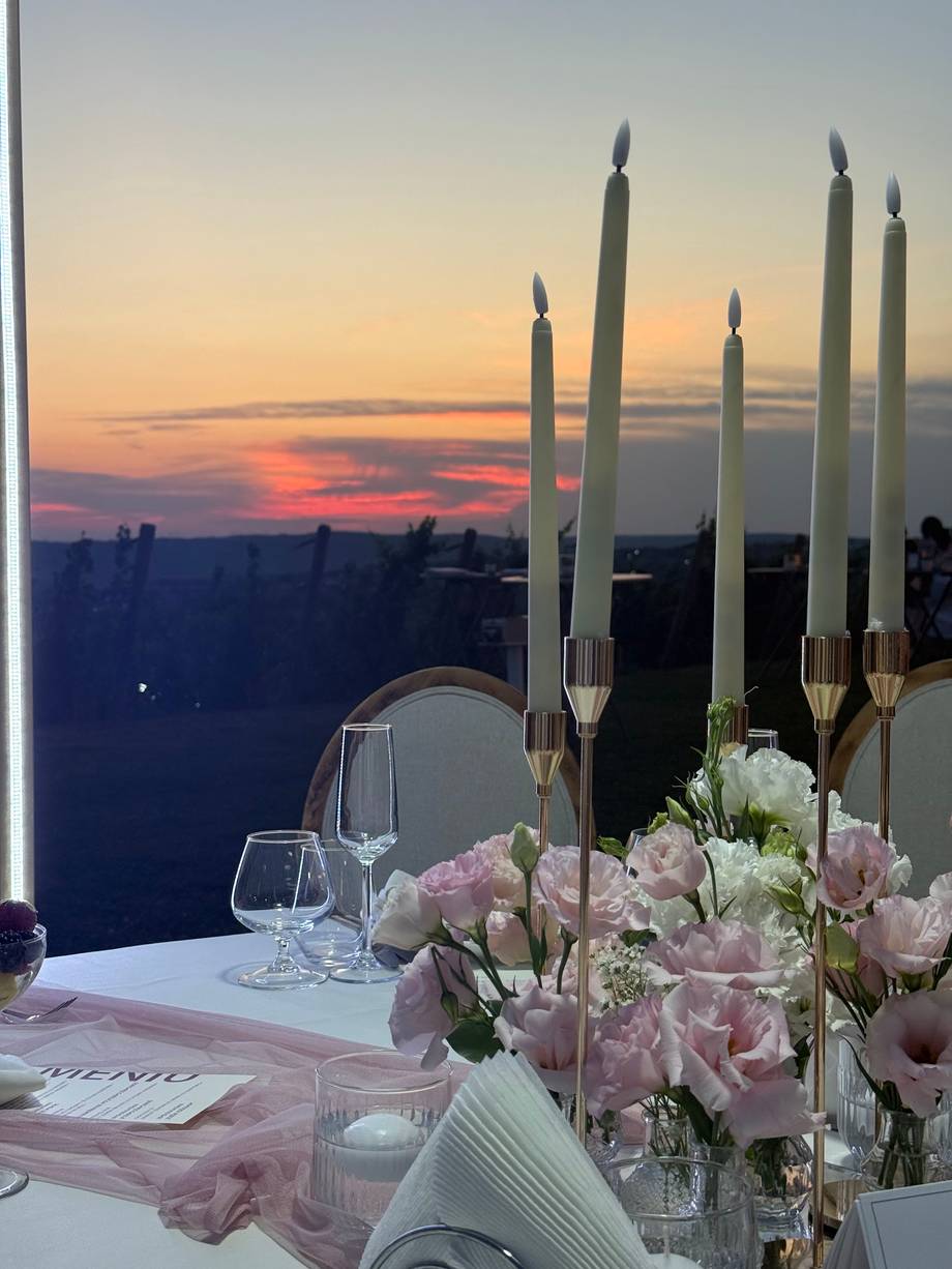 Elegant dinner table setting with tall candles, pink flowers, and sunset cityscape view