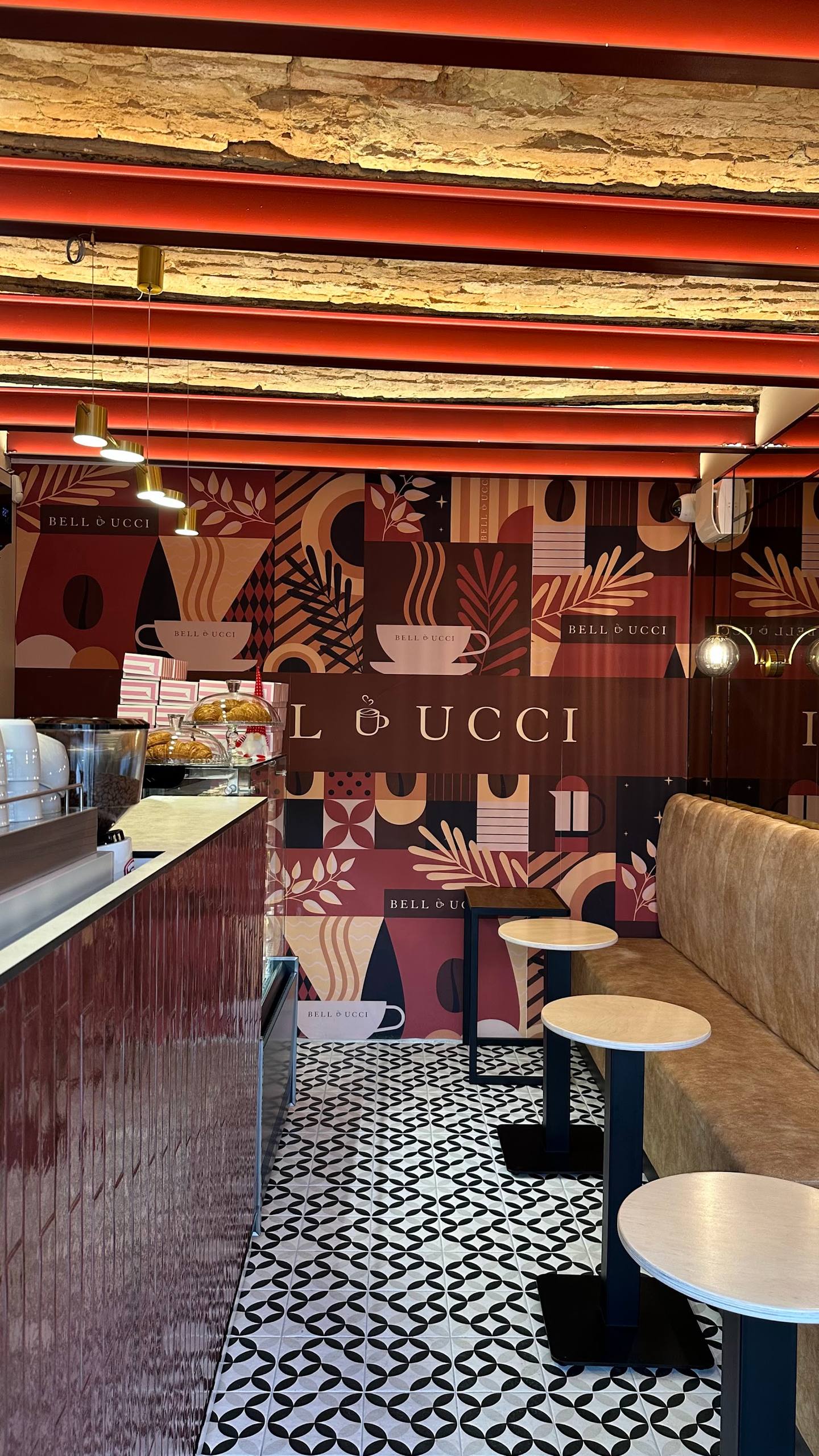 Modern café interior with signature branding, geometric floor tiles, booth seating, and red beam ceiling details