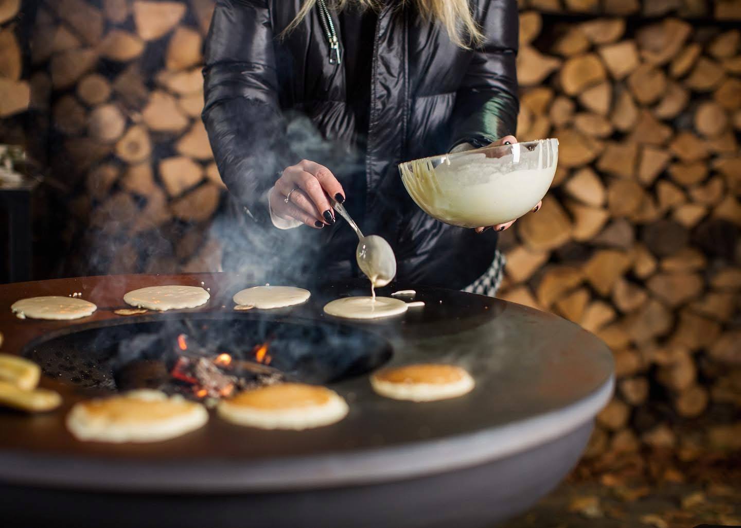 Chef plating crepes at a rustic fireplace venue with stacked wood backdrop