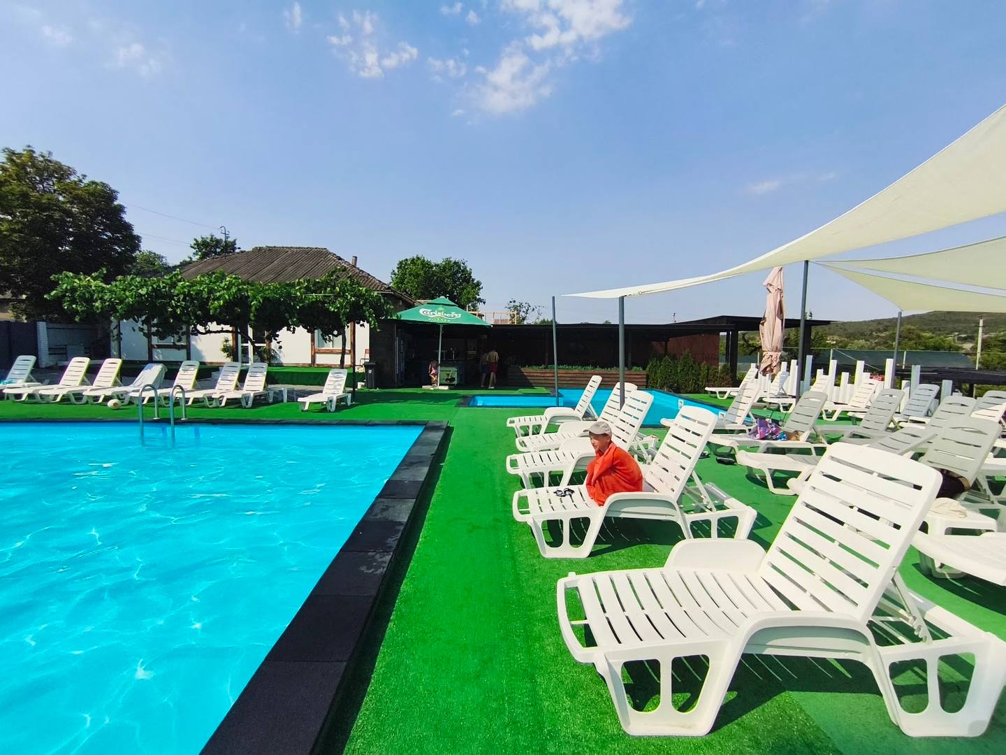 Outdoor pool area with sunbeds, green lawn, and shade canopy on bright sunny day