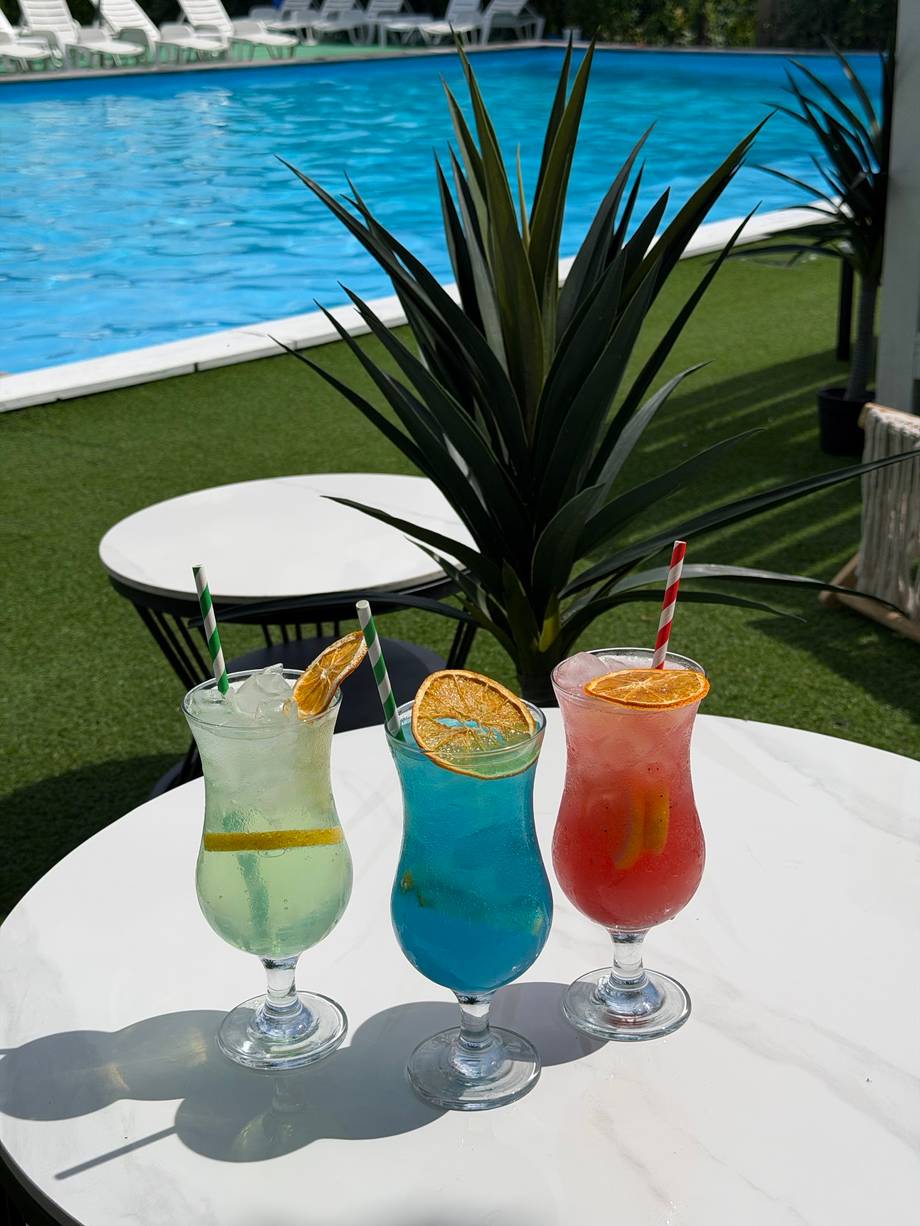 Three signature cocktails by the pool with loungers and lush landscaping