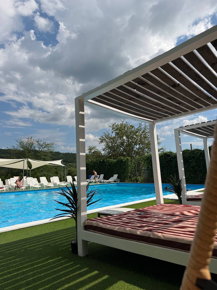 Modern poolside terrace with pergolas, loungers, and resort pool under blue sky