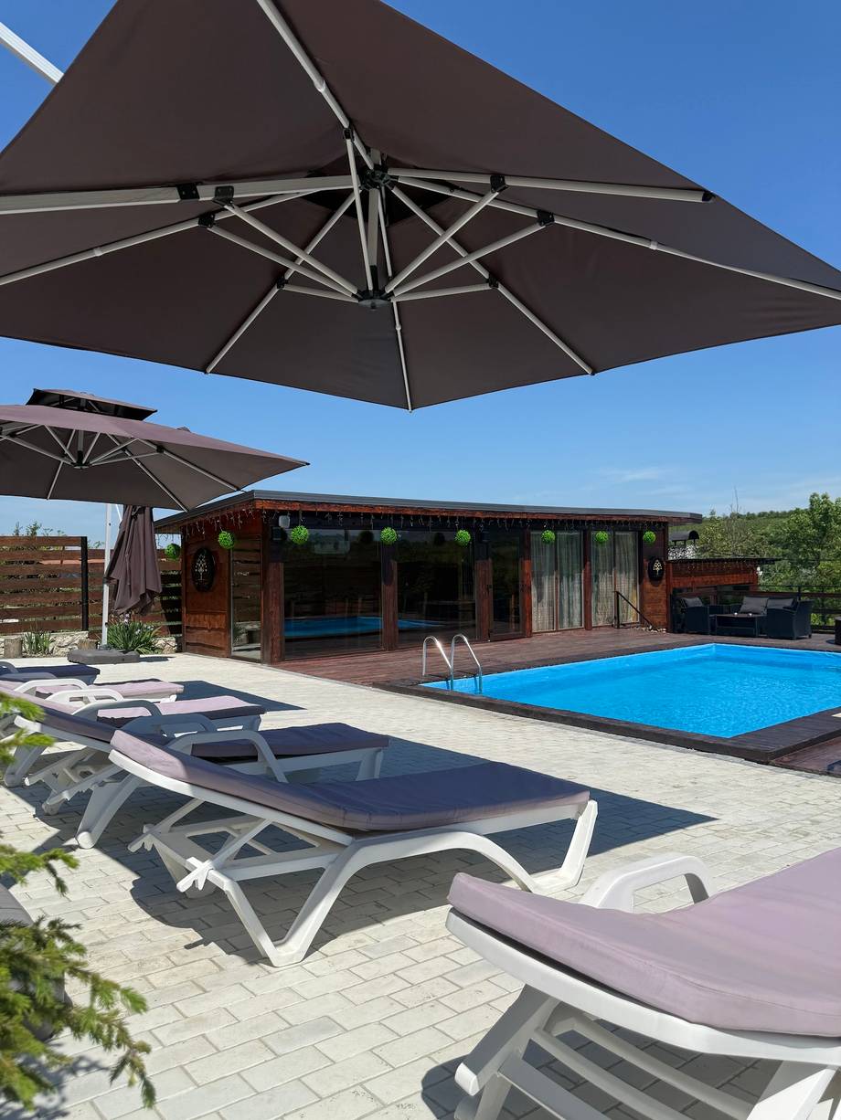 Outdoor terrace with pool, lounge chairs, umbrellas and modern pavilion building under clear sky