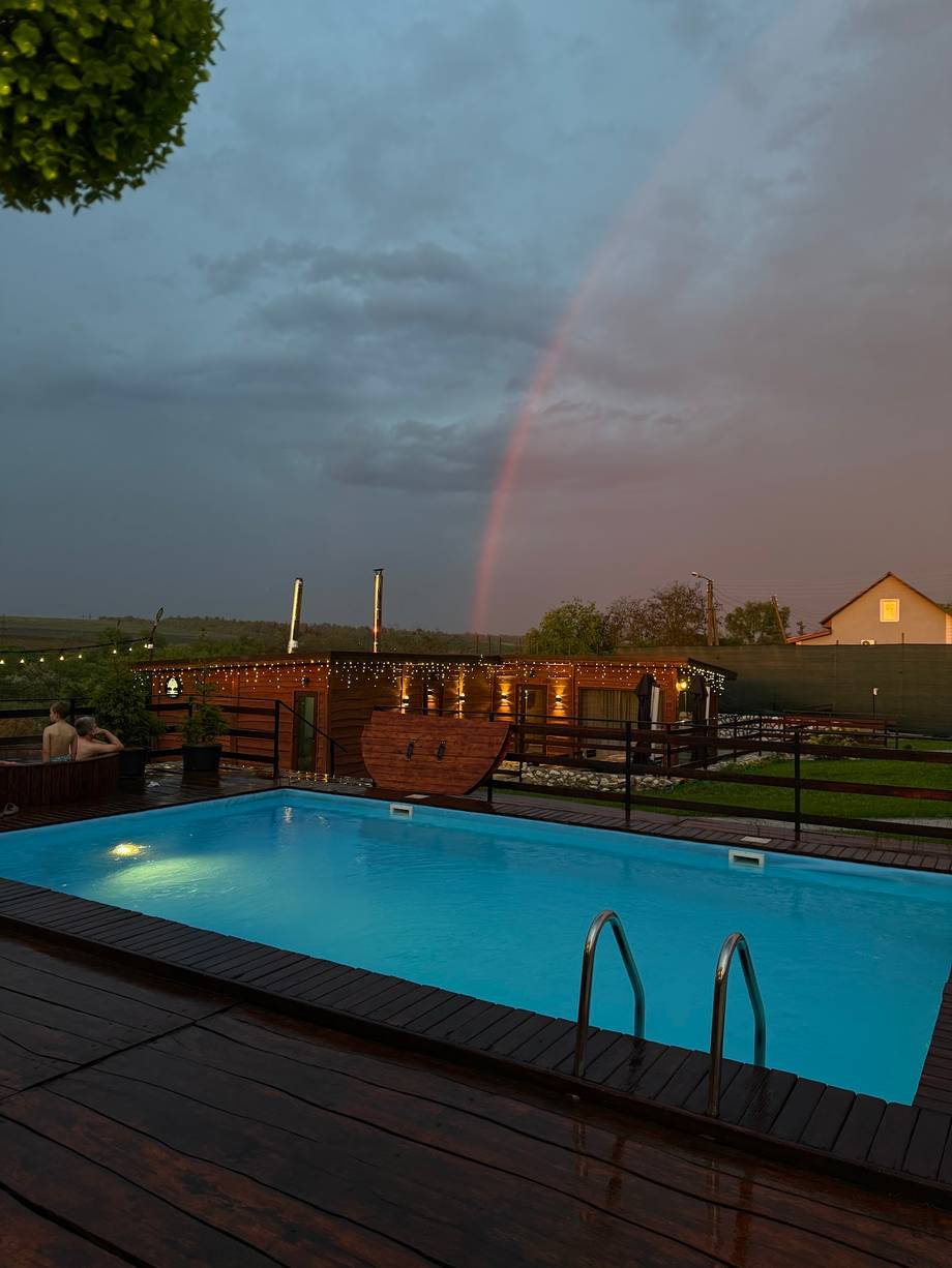 Illuminated outdoor pool at dusk with rainbow and rural architecture backdrop