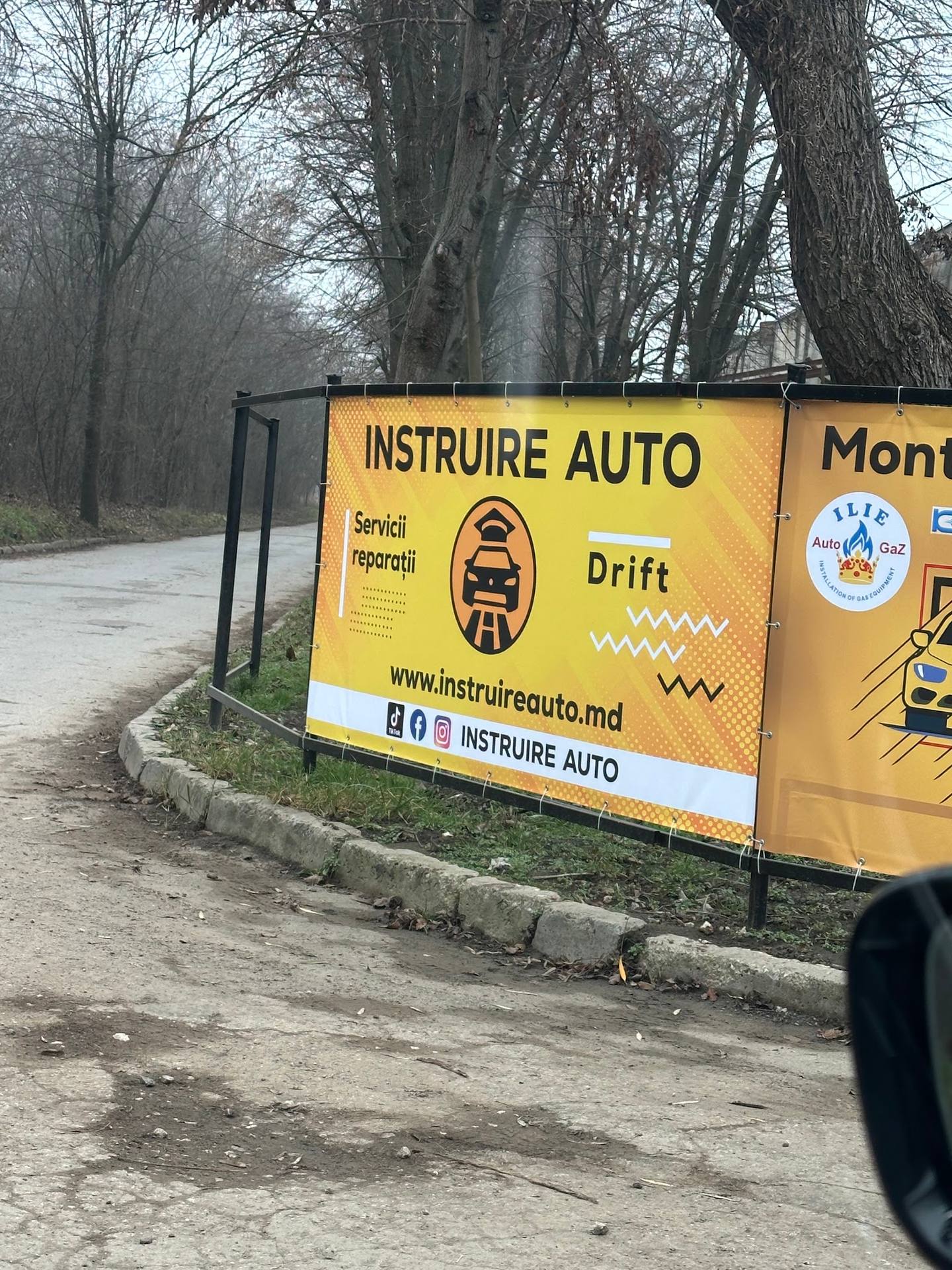 Instruire Auto signage on roadside with bare trees in background