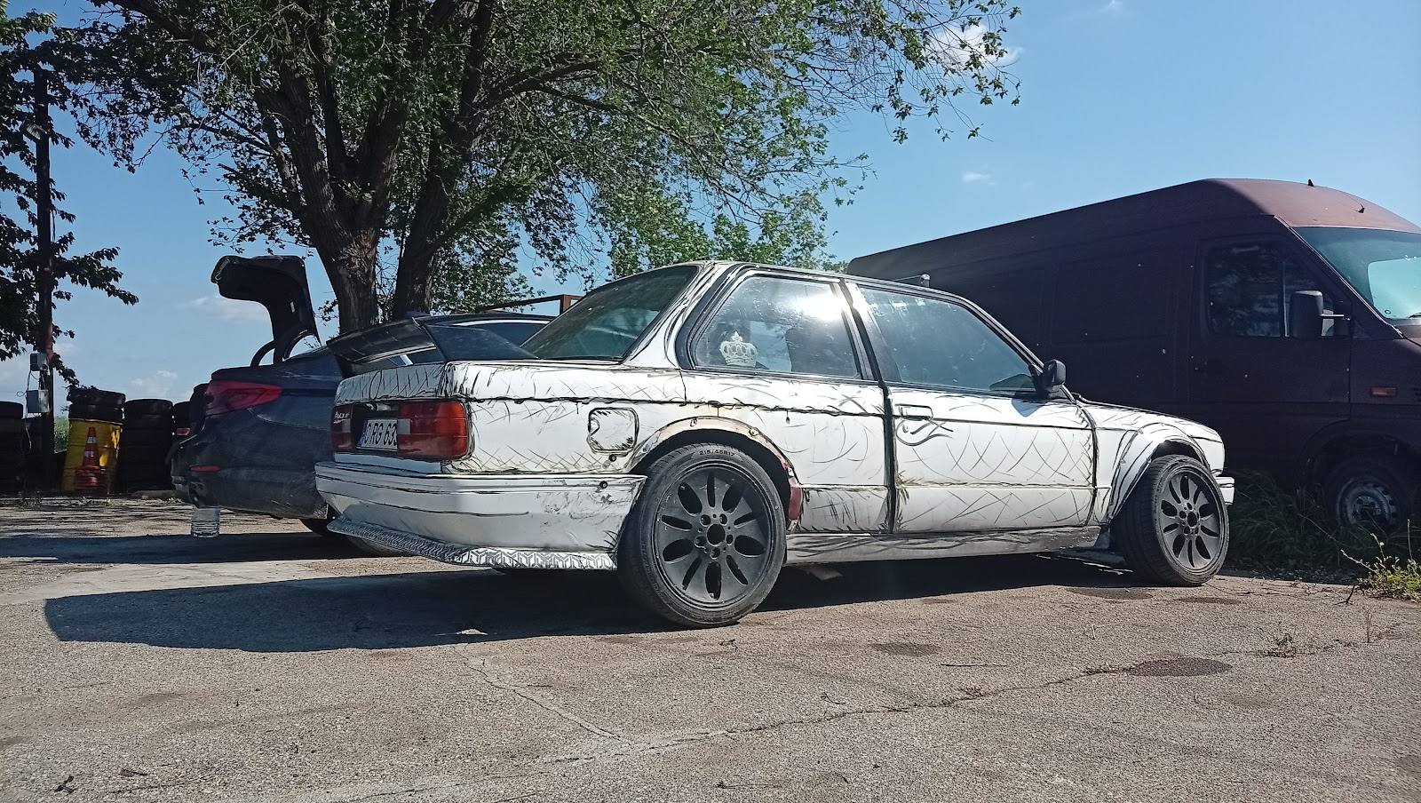 Damaged white sedan parked near scrap metal structure