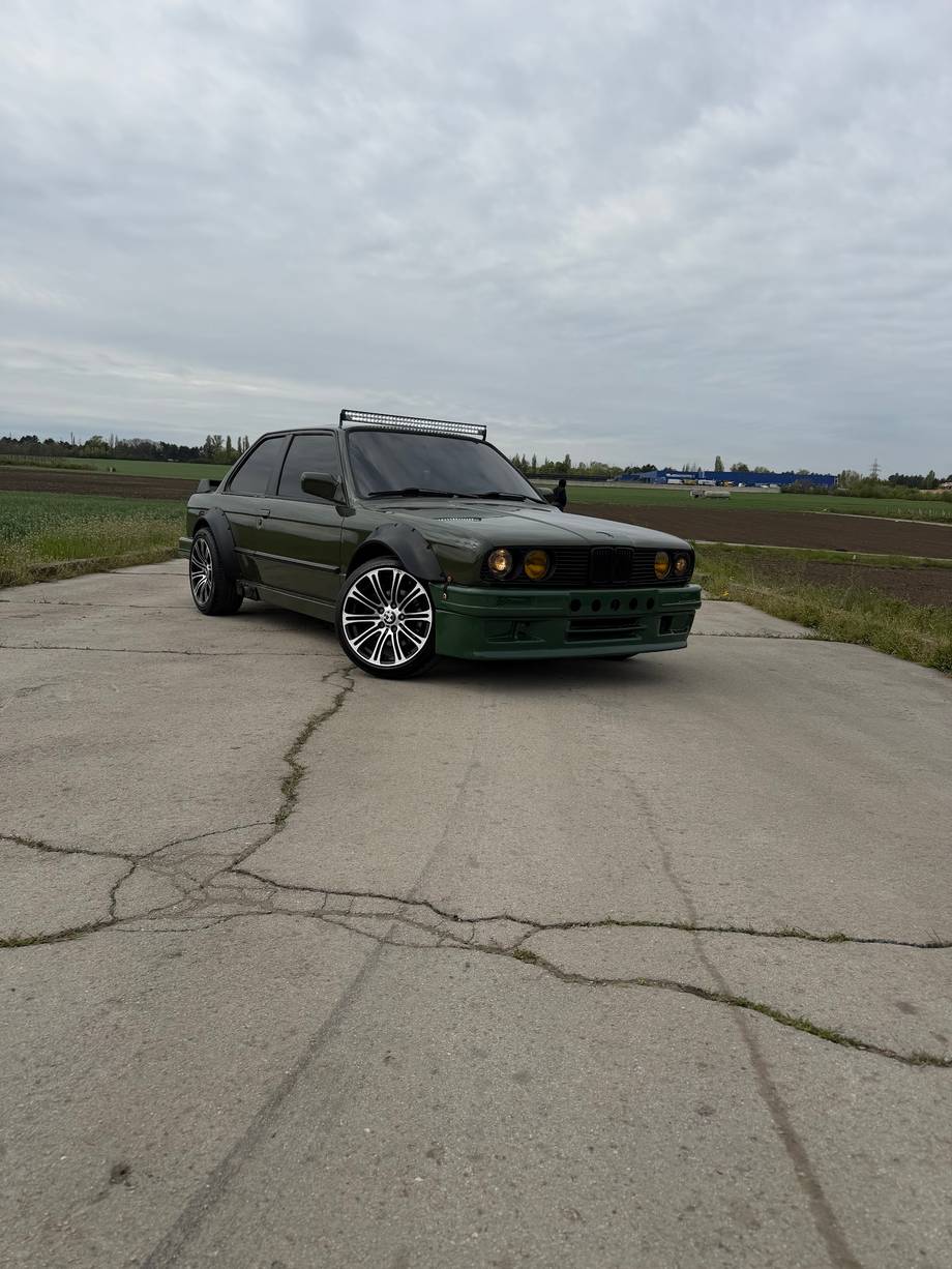 Green modified sedan on rural road with open fields