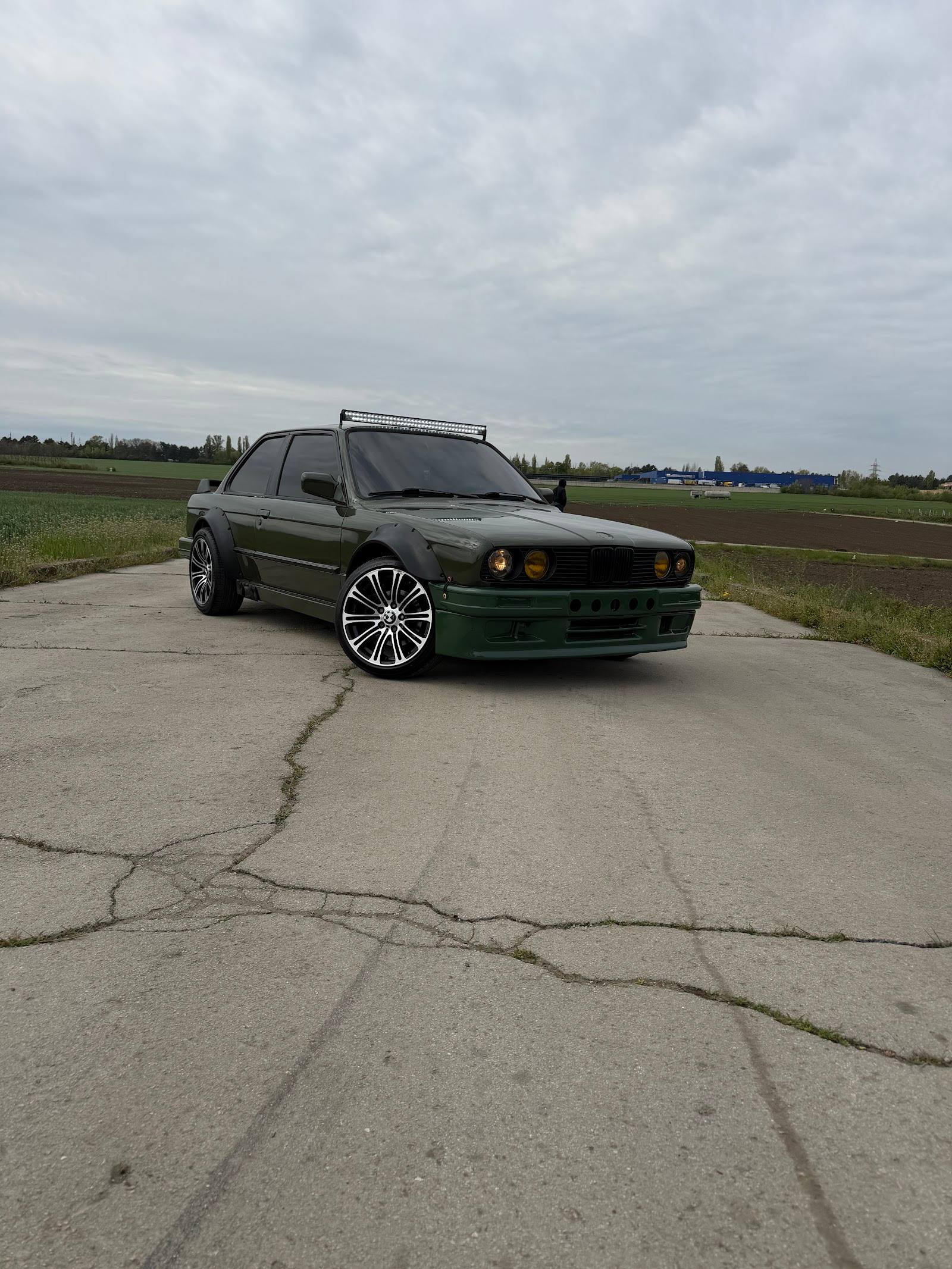 Green modified sedan on rural road with open fields