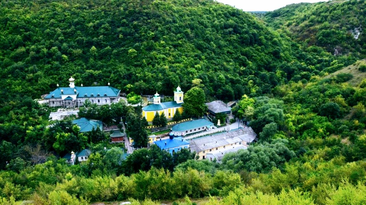 Aerial view of monastery complex nestled in forested mountains with distinctive blue and yellow domes