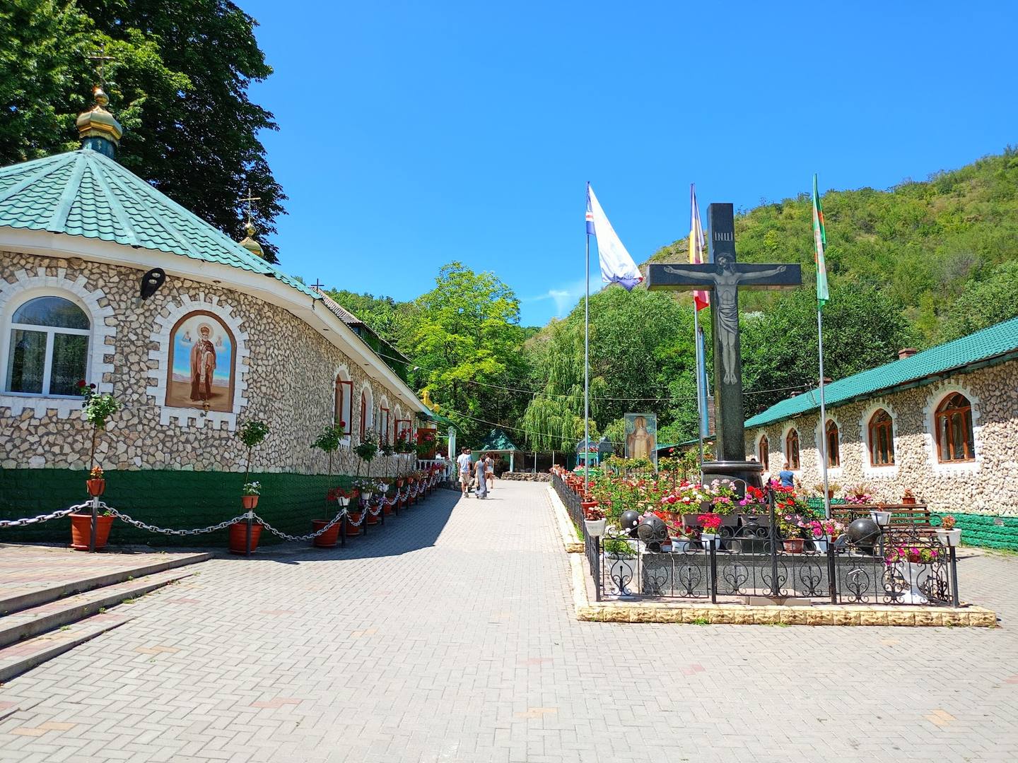 Stone monastery with copper dome and large cross in verdant hillside setting