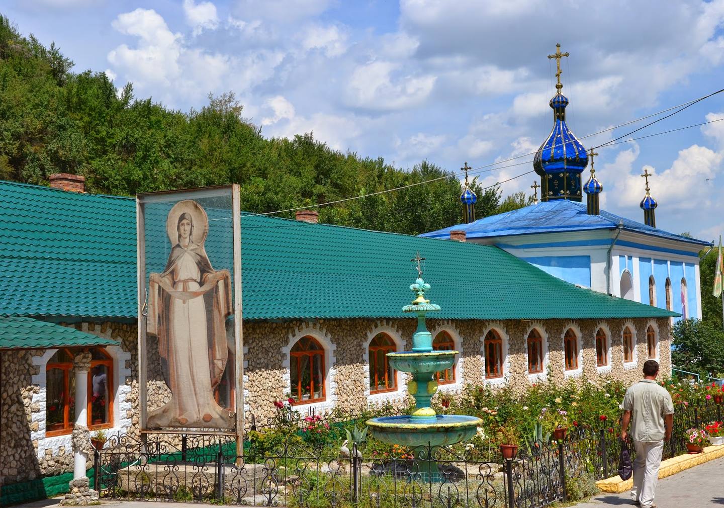 Stone monastery with distinctive blue domed roof and bell tower, framed by greenery