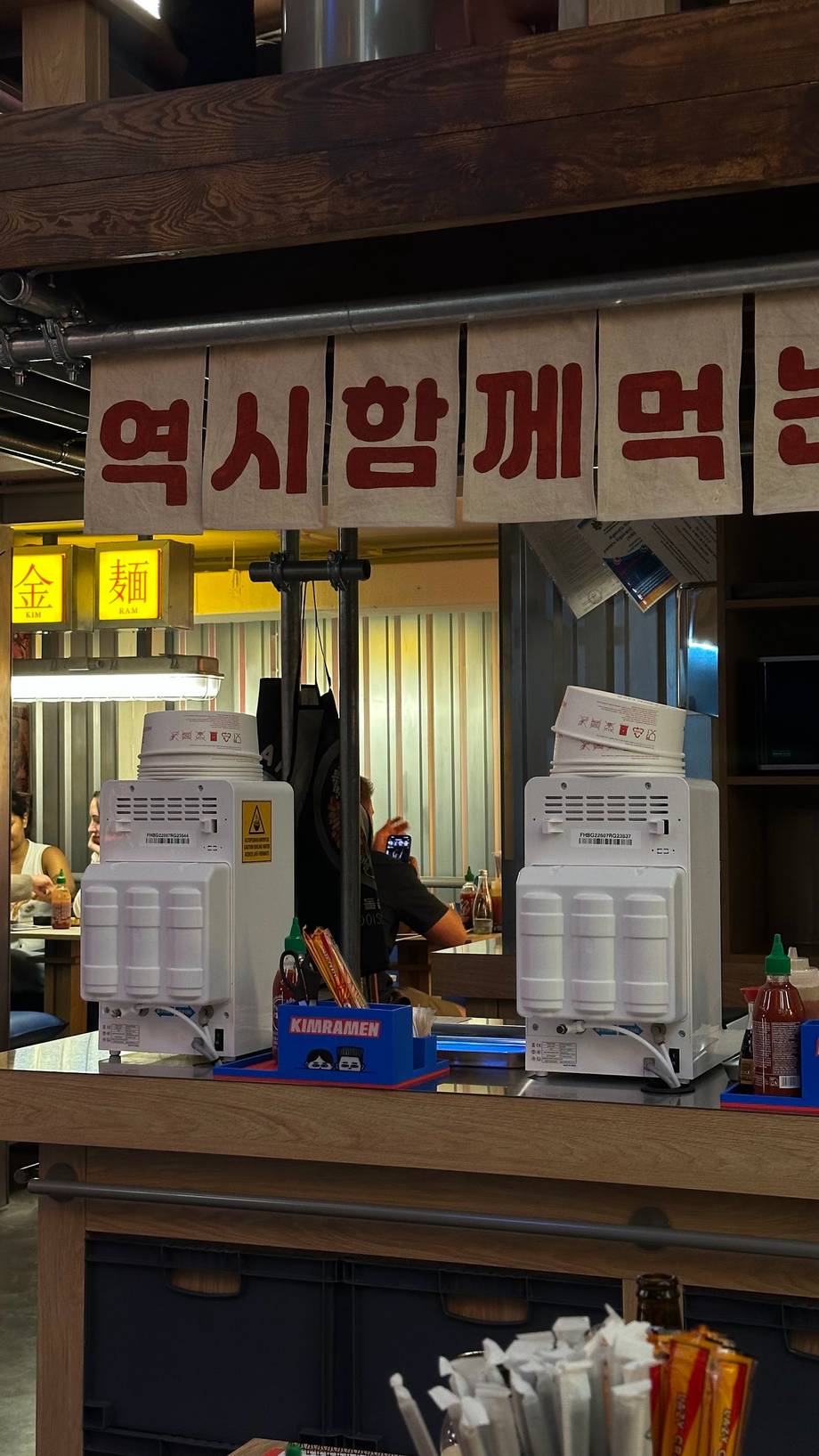 Korean food stall counter with signage and beverage dispensers during service
