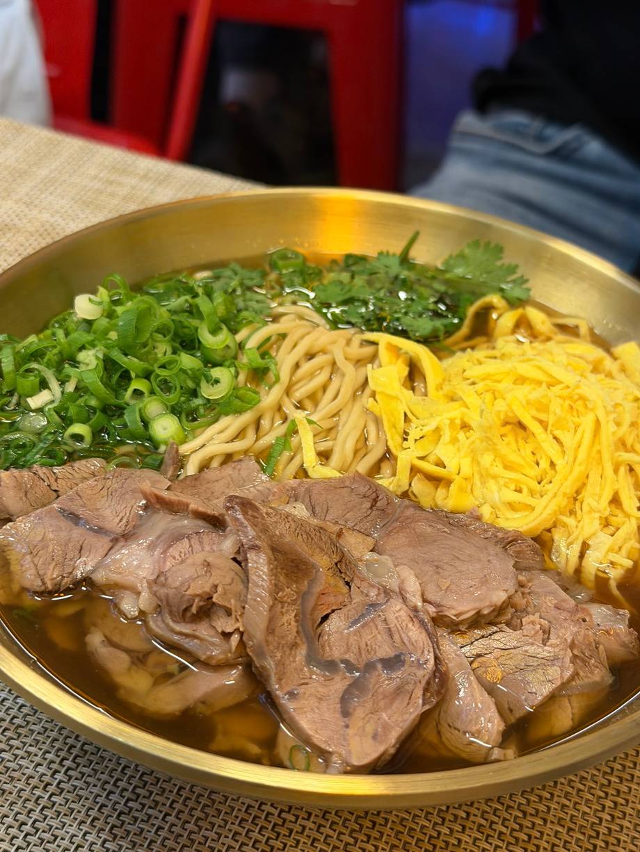 Ramen bowl with beef slices, yellow noodles, and fresh greens