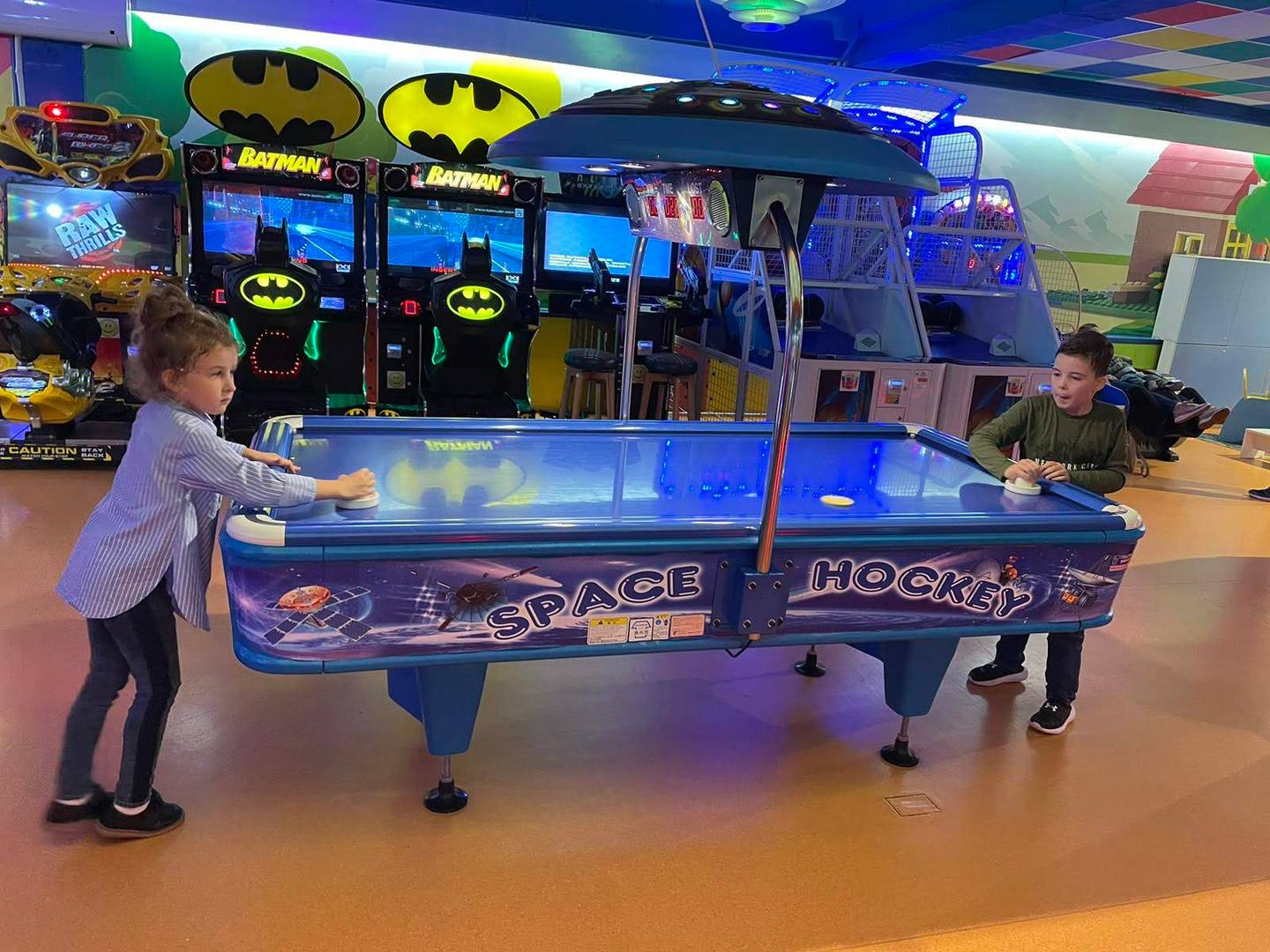Air hockey game with arcade and Batman games visible in entertainment venue