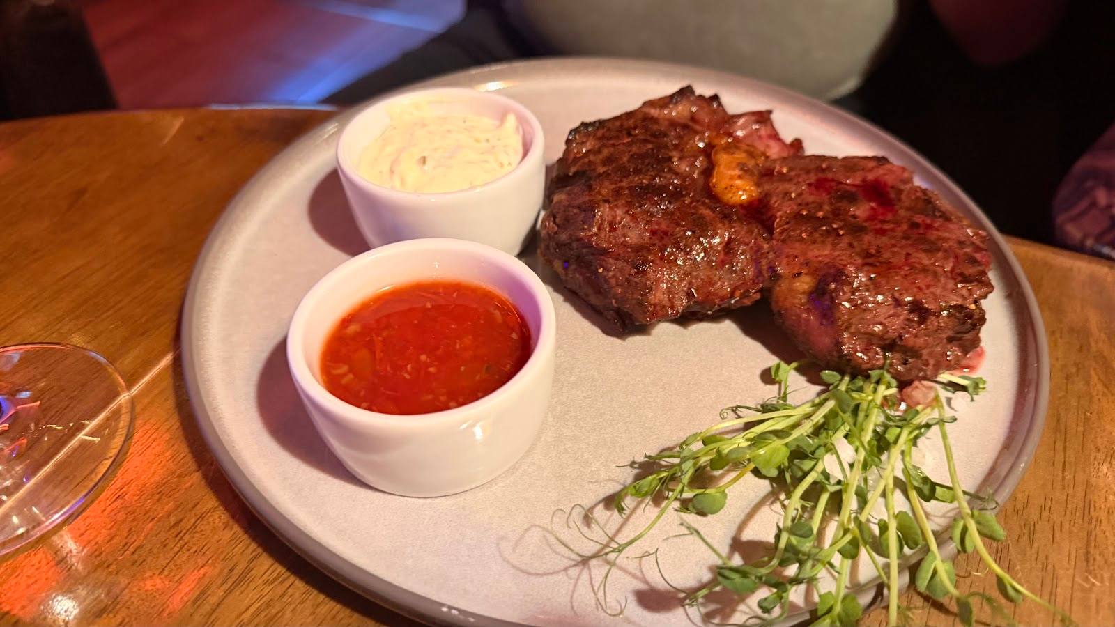 Grilled steak with herb garnish and sauce accompaniments on white plate
