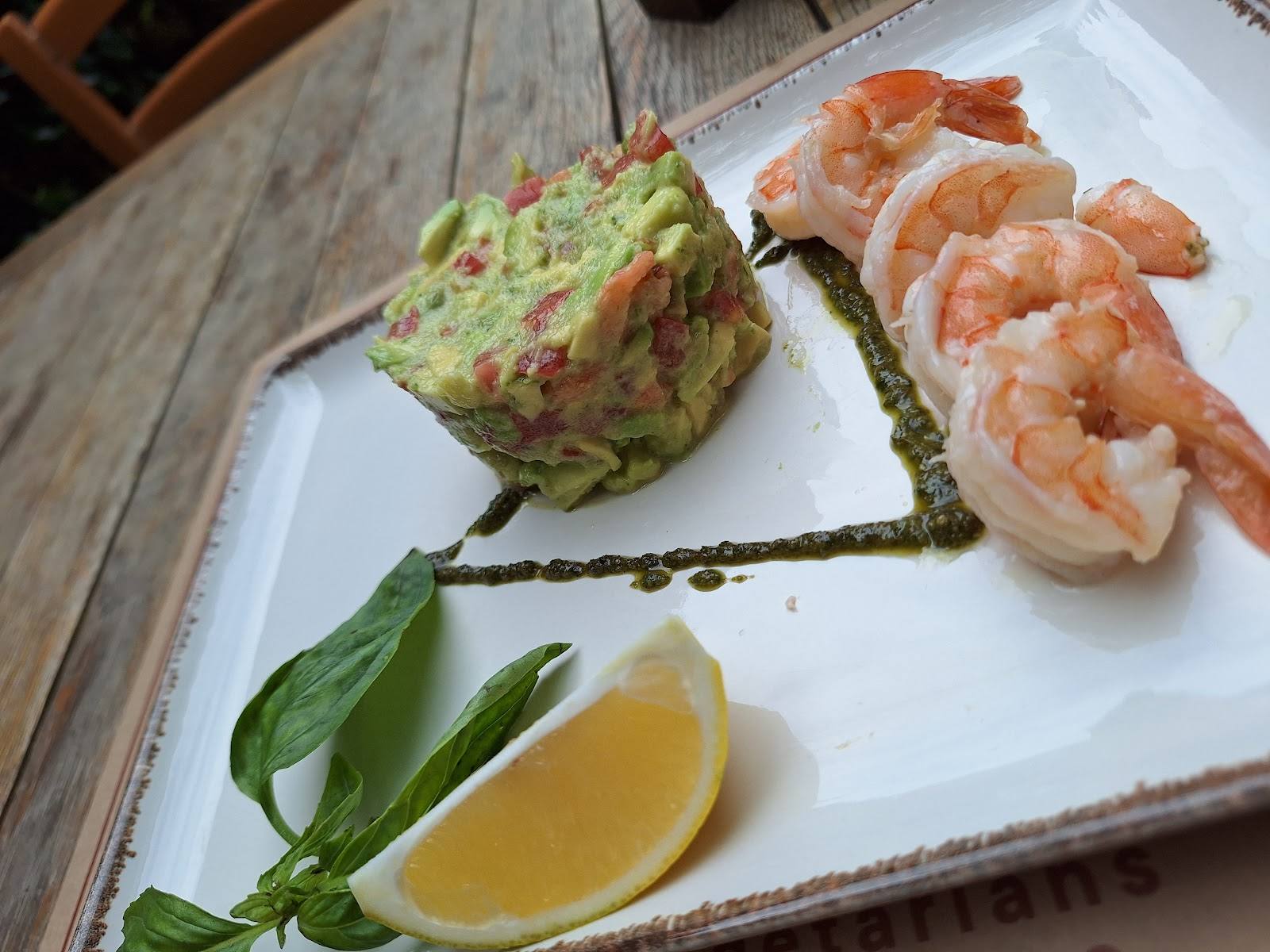 Plated appetizer with guacamole, shrimp, and lemon on white ceramic