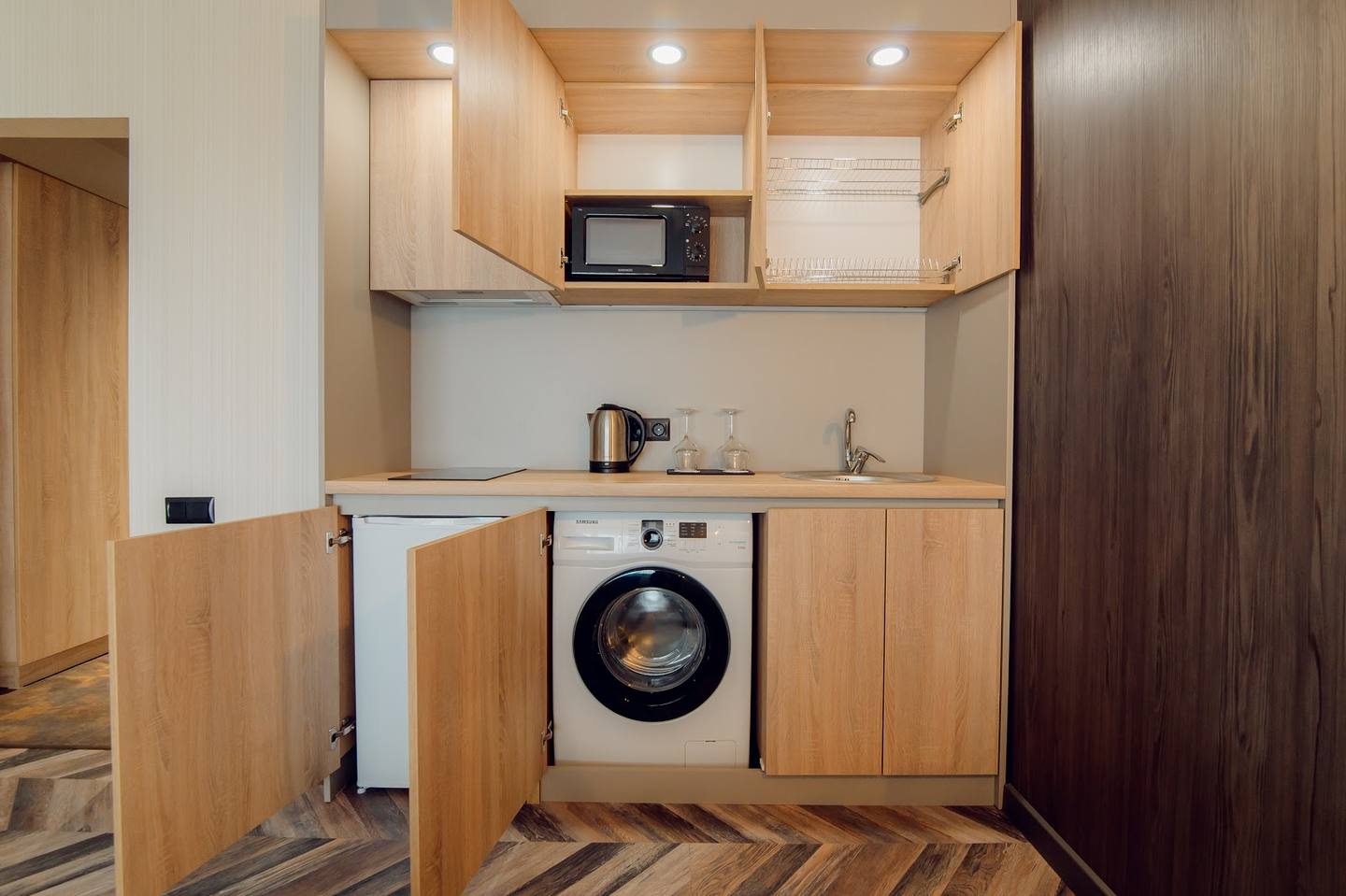 Compact kitchenette with wood cabinetry and integrated washing machine